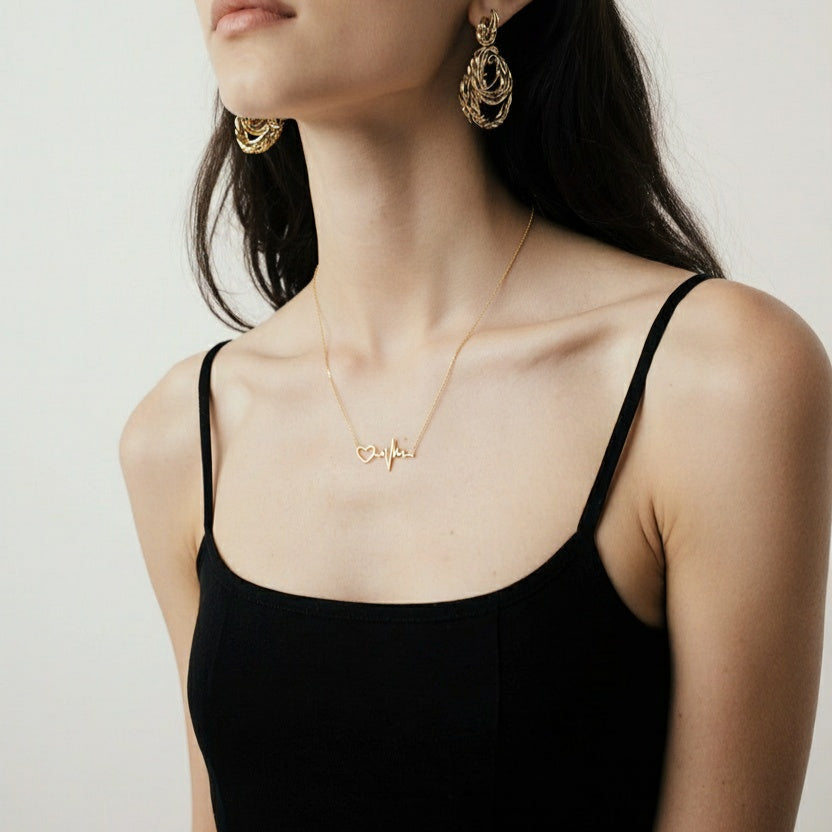Woman wearing a gold necklace with a heart design on a plain background