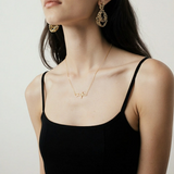Woman wearing a gold necklace with a heart design on a plain background