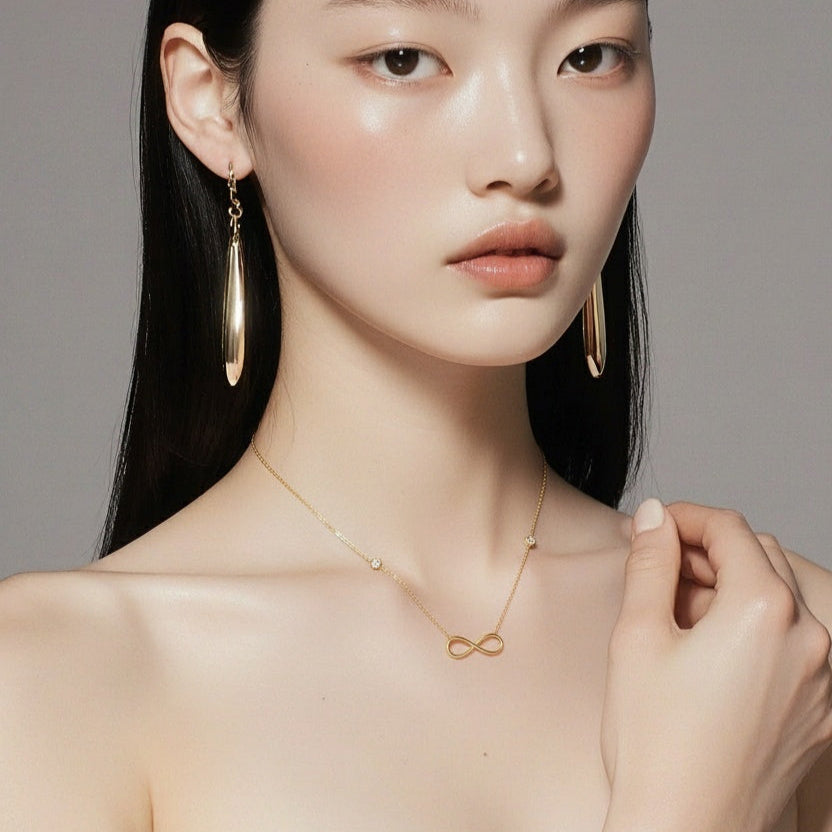 woman wearing 14k solid yellow gold infinity necklace with bezel set zircon on a gray background by Qutahia Jewelry
